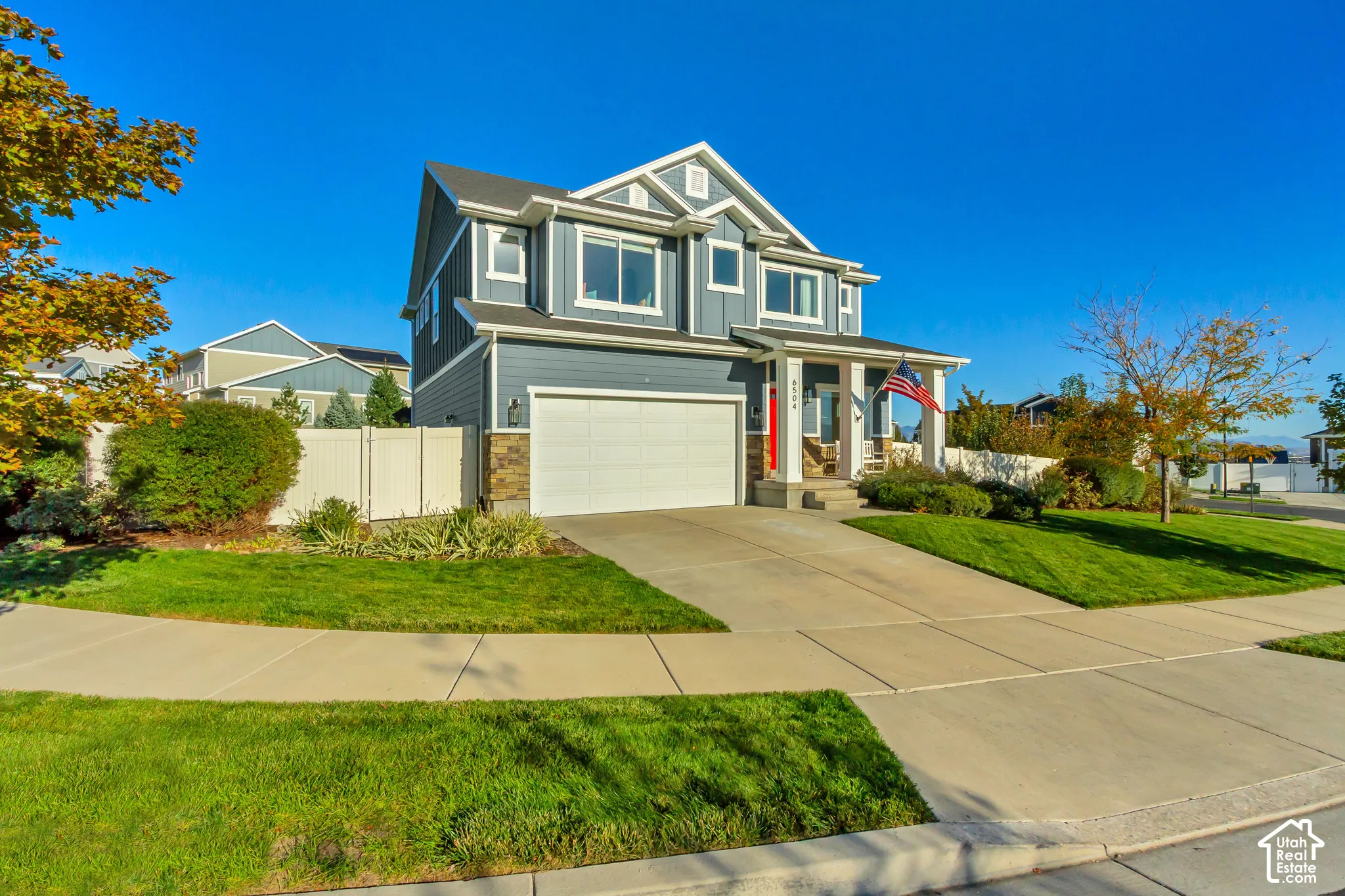Two-story residence featuring full wrap gray James Hardie cement board siding with stone veneer accents, a covered front porch, a red entry door, and a two-car garage