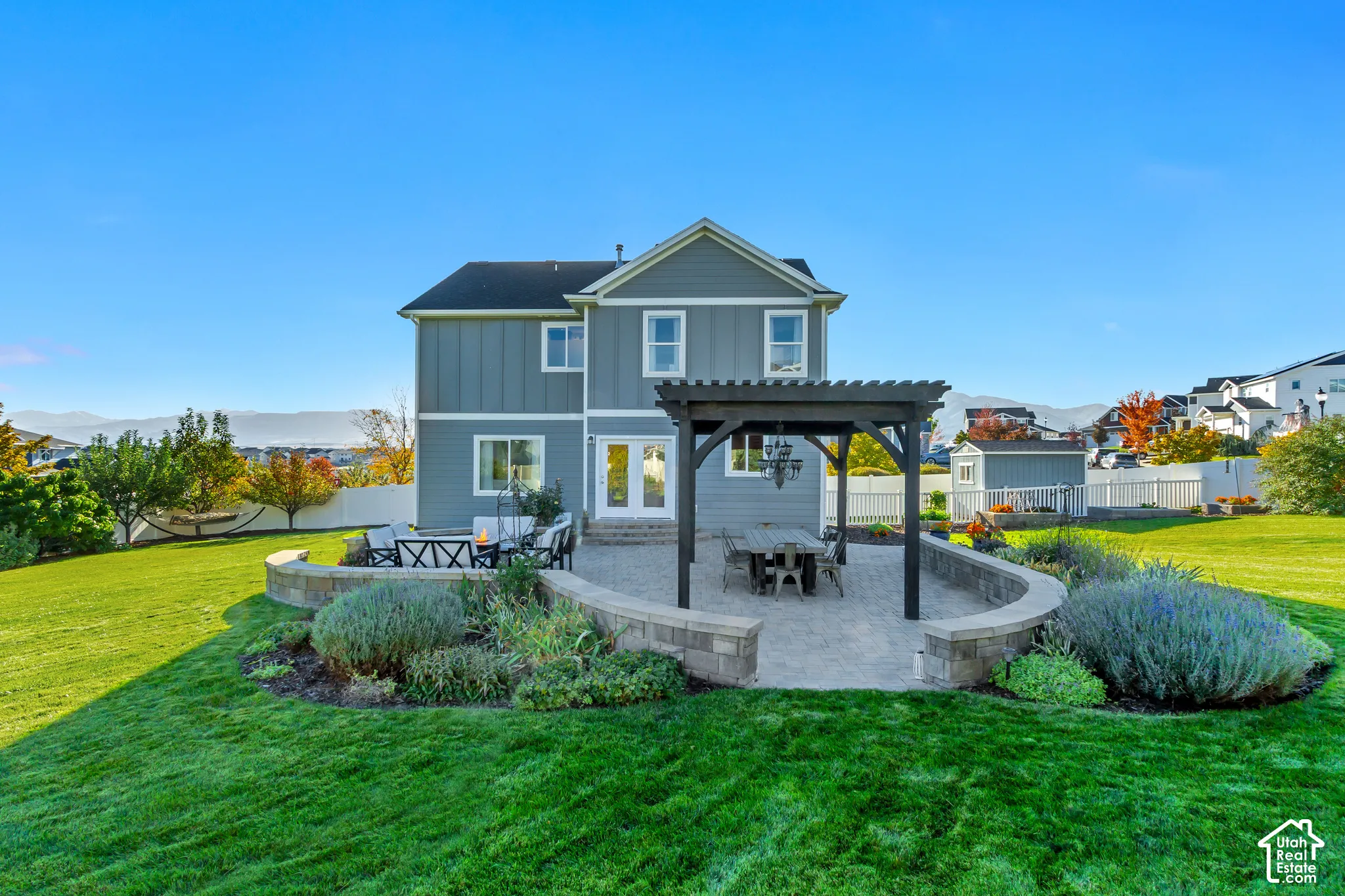 Backyard patio featuring pavers, a Western Timberframe wooden pergola, and a curved stone retaining wall surrounded by beautifully planted garden beds and an expansive grass lawn