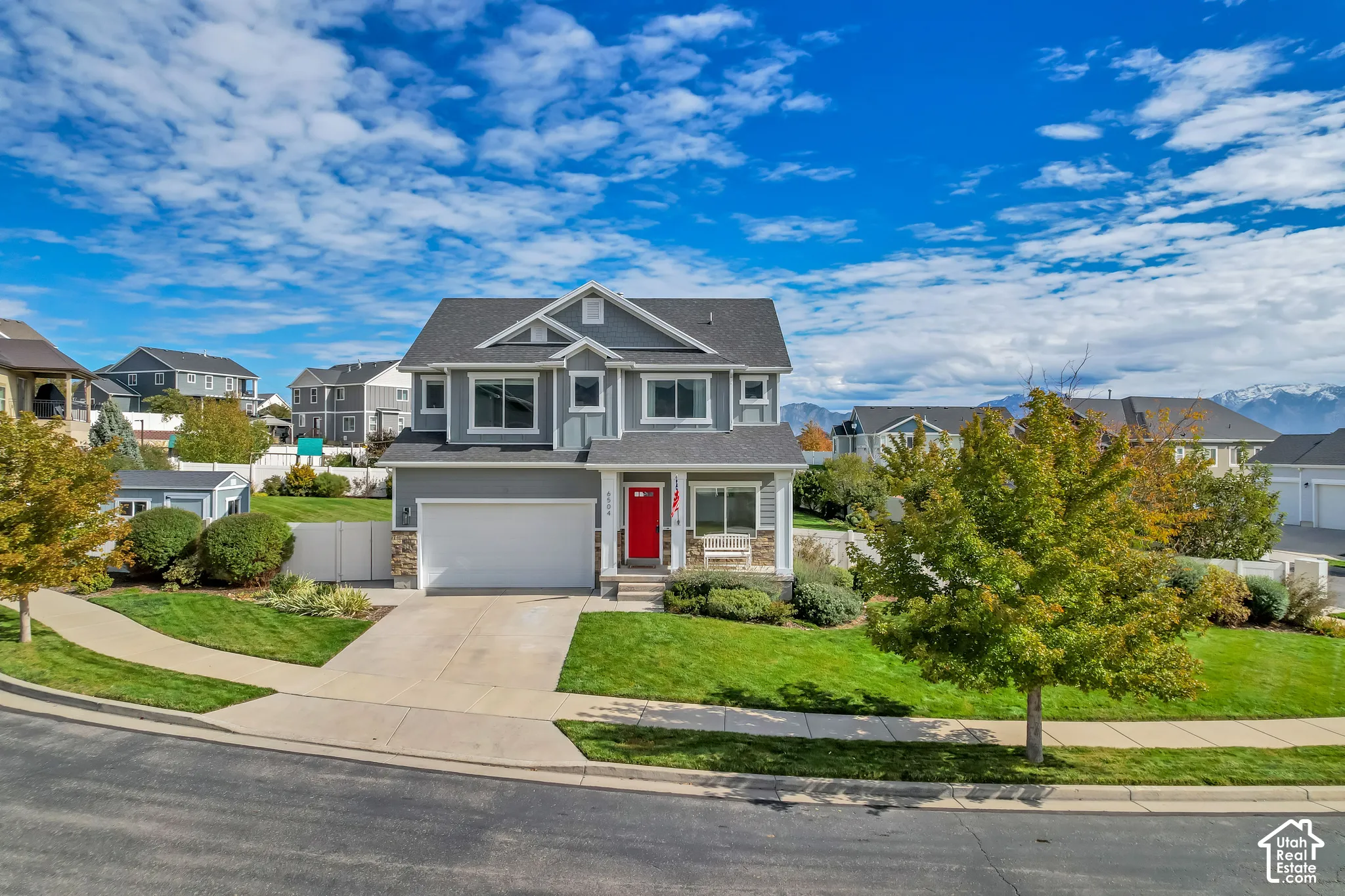 Two-story exterior featuring fiber-cement siding, stone veneer accents, an attached two-car garage, a covered front porch with square columns, and a bright red entry door