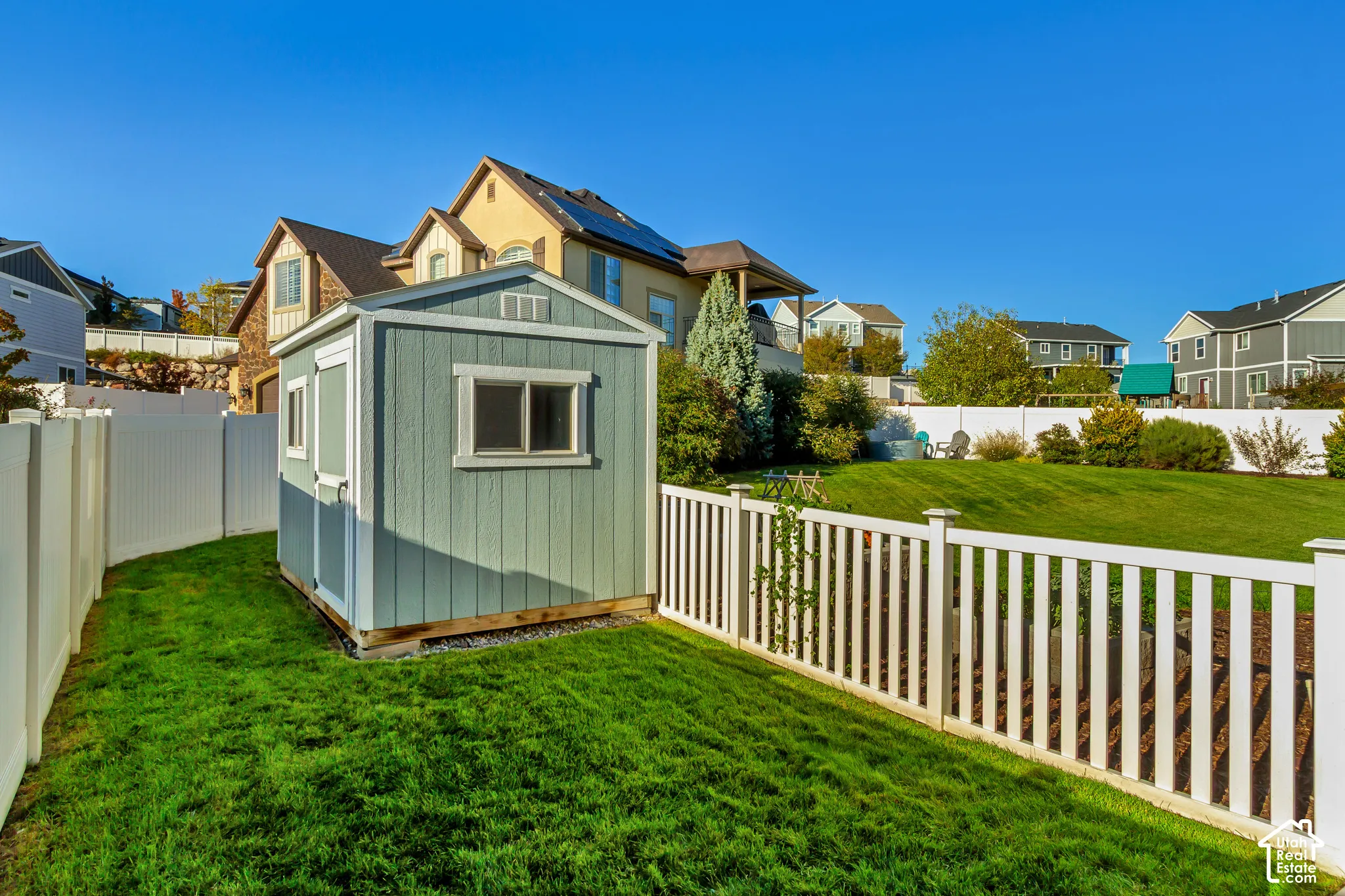 Backyard featuring a dog run, detached storage shed, white vinyl privacy fencing, manicured lawn, and mature landscaping