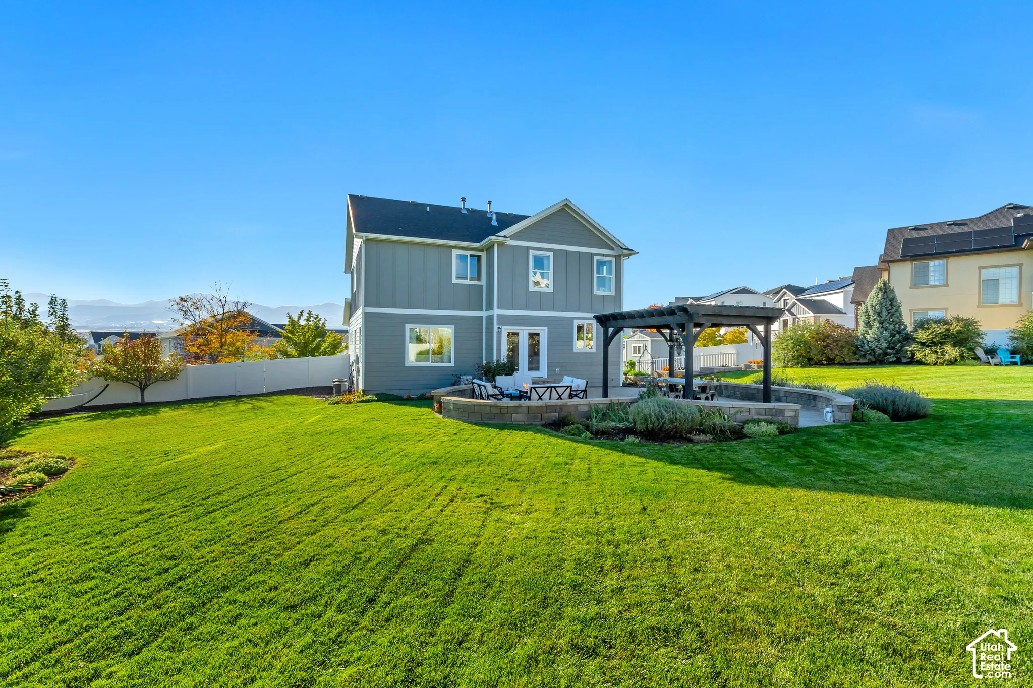 Backyard patio featuring pavers, a Western Timberframe wooden pergola, and a curved stone retaining wall surrounded by beautifully planted garden beds and an expansive grass lawn
