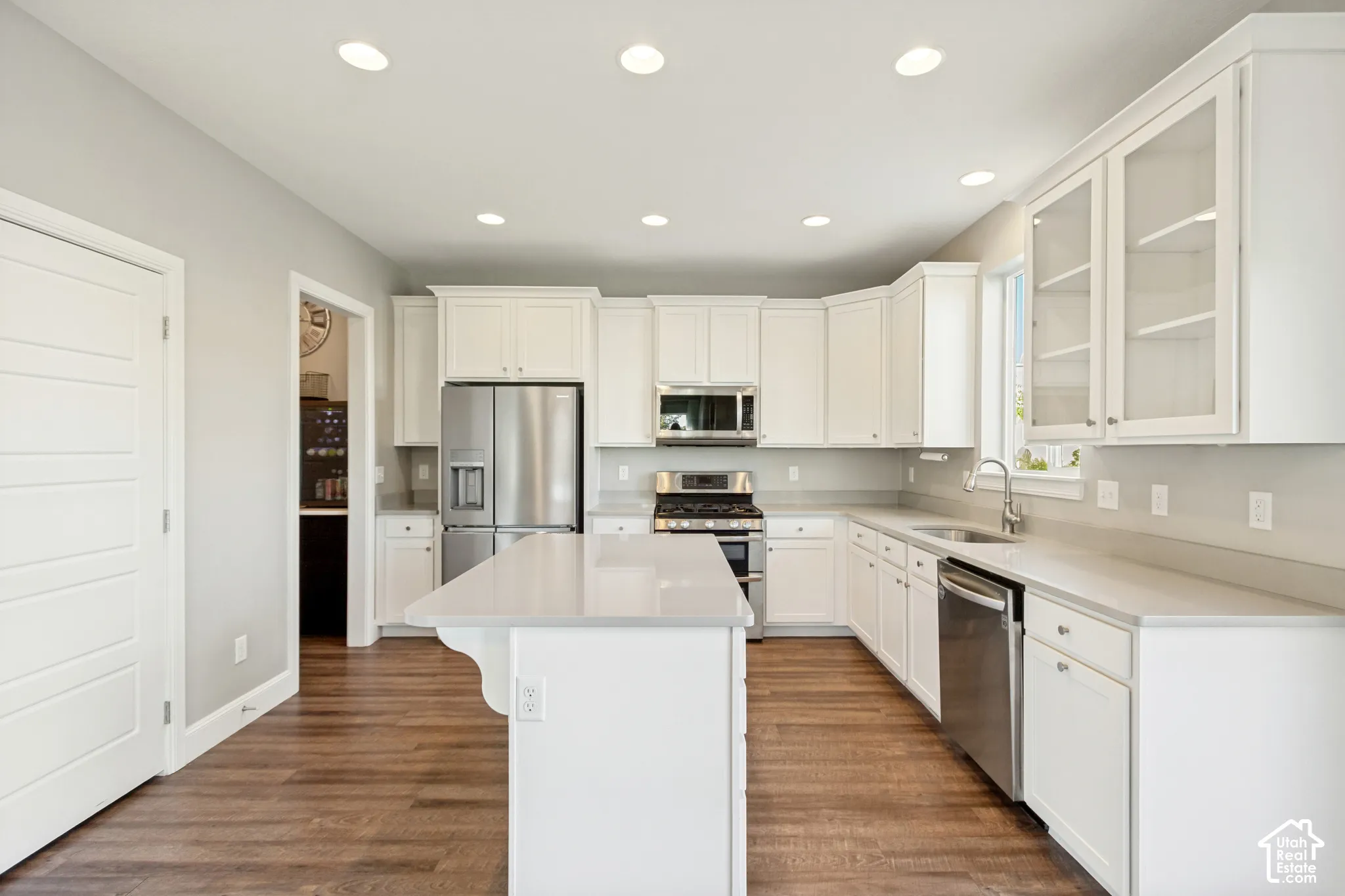 Kitchen featuring wonderful natural light, white shaker-style cabinetry with glass-front display uppers, expansive center island, quartz countertops, stainless steel appliances, and LVP flooring