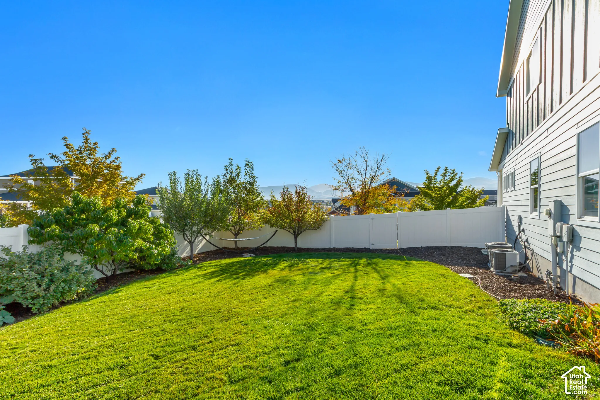 Backyard patio featuring pavers, a Western Timberframe wooden pergola, and a curved stone retaining wall surrounded by beautifully planted garden beds and an expansive grass lawn