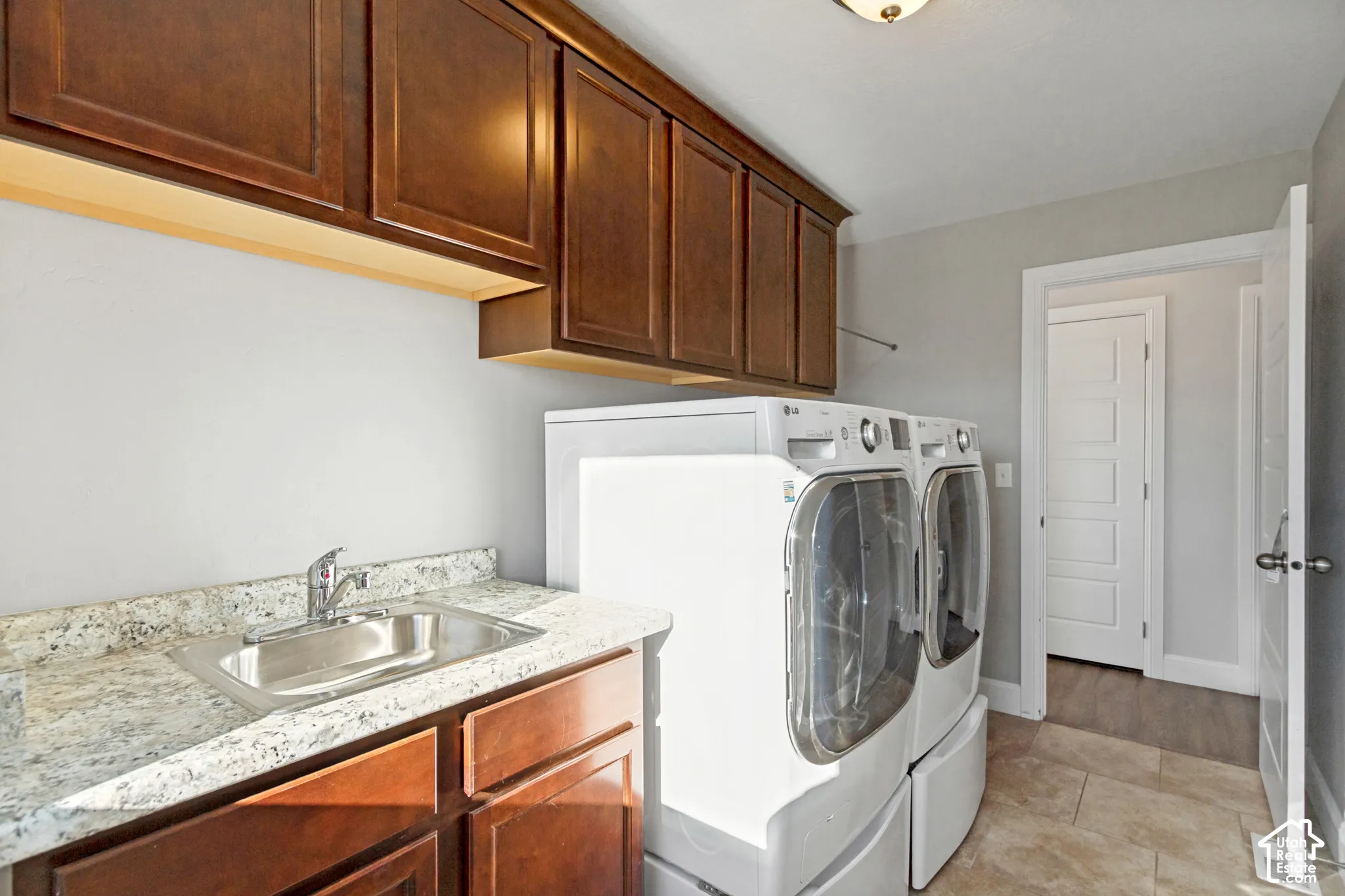 Laundry area featuring dark-stained wood cabinetry, a laundry sink, tiled flooring, and a window with mountain scenery
