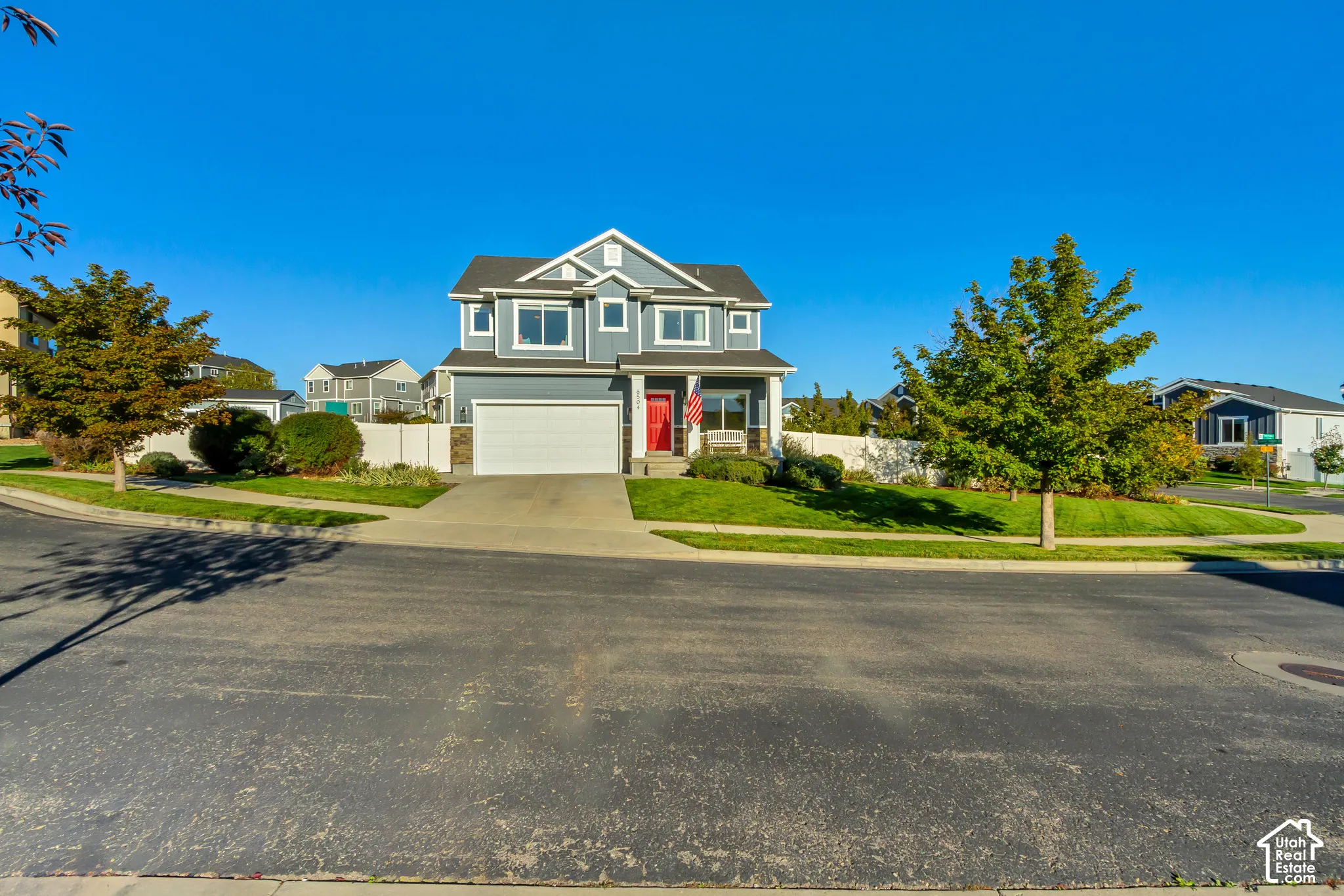 Two-story residence featuring full wrap gray James Hardie cement board siding with stone veneer accents, a covered front porch, a red entry door, and a two-car garage