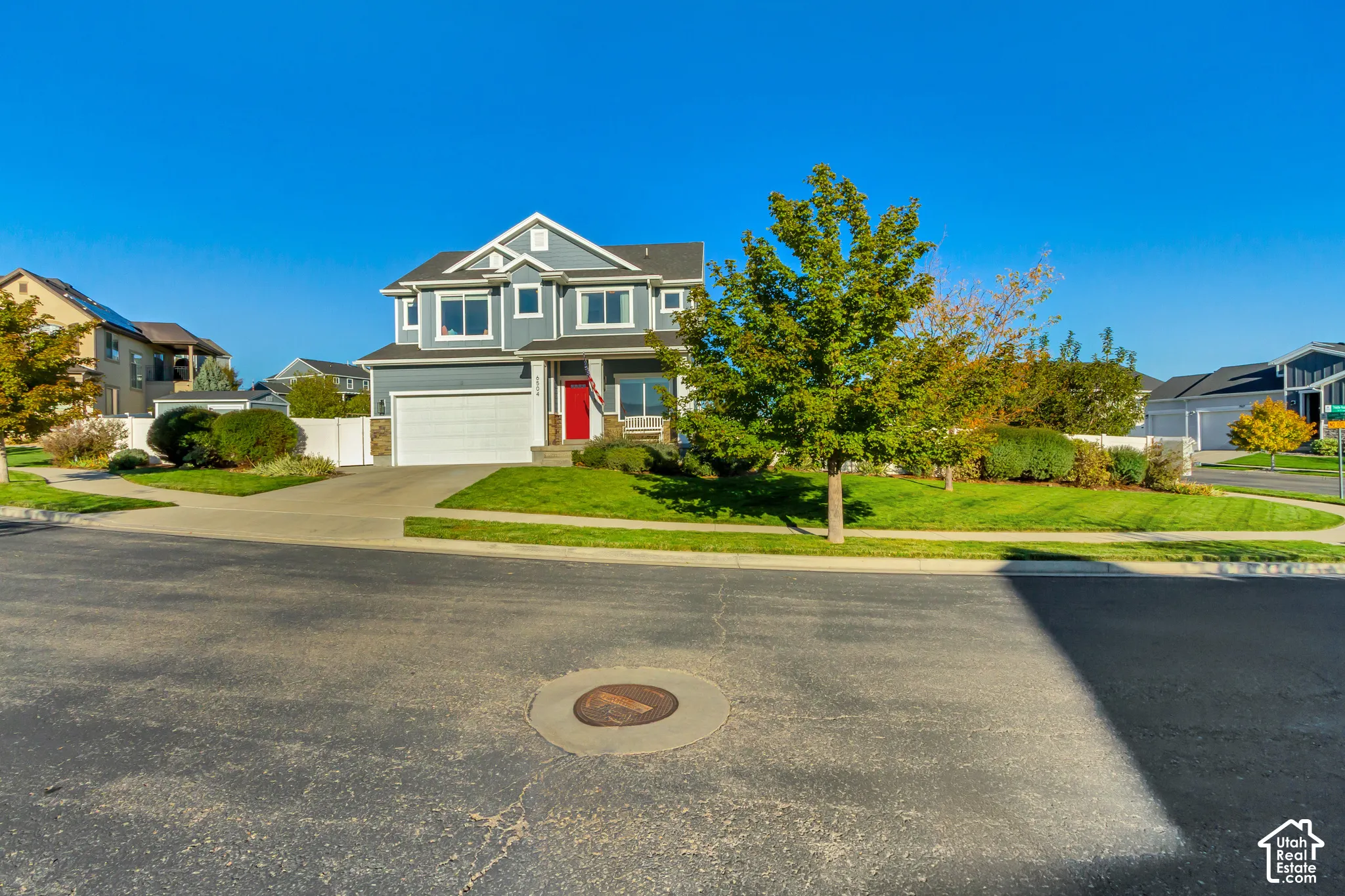 Two-story residence featuring full wrap gray James Hardie cement board siding with stone veneer accents, a covered front porch, a red entry door, and a two-car garage