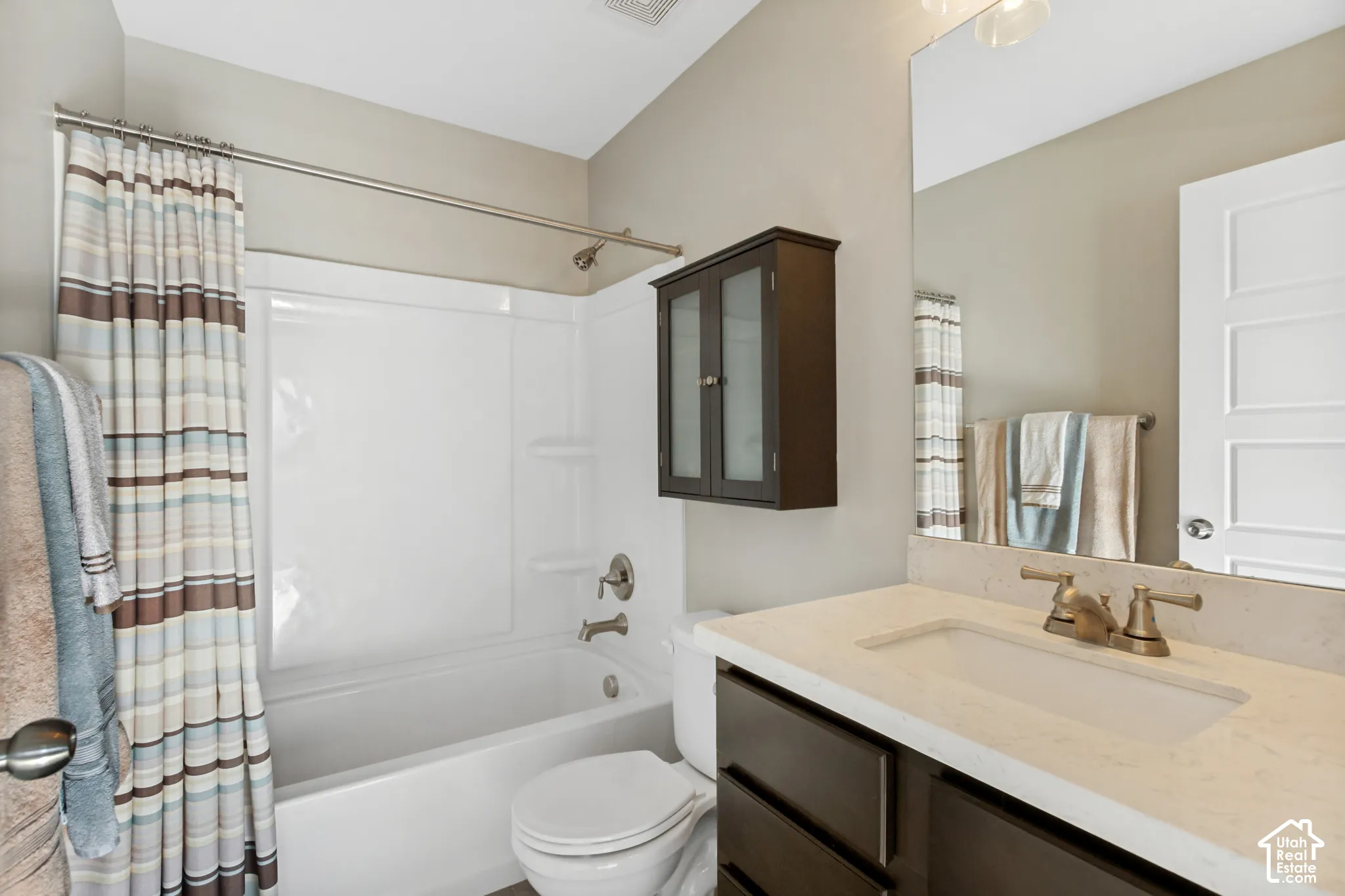 Bathroom featuring a light-toned solid surface vanity countertop with an integrated rectangular sink, dark wood-finish cabinetry, a large wall-mounted mirror, and a full-height shower and tub surround