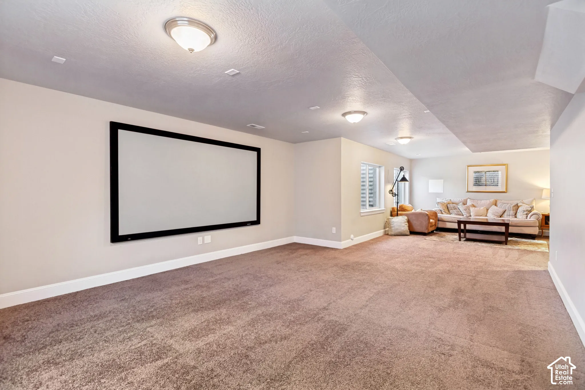 Open-concept basement perfect for entertaining featuring carpeted flooring, built-in projection screen and prewired for a home theater and plumbed foir a wet bar, multiple egress windows with window wells provide plenty of light
