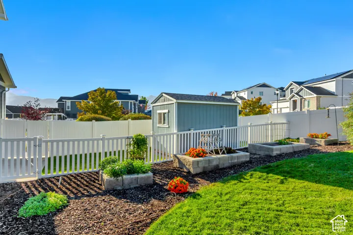 Backyard featuring a white vinyl privacy fence, Tuff Shed, raised masonry garden beds, and manicured lawn