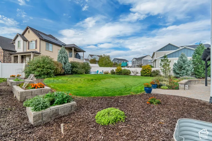 Expansive backyard featuring a manicured lawn, established landscaping, raised garden beds including an herb garden, a paver patio, and a privacy fence