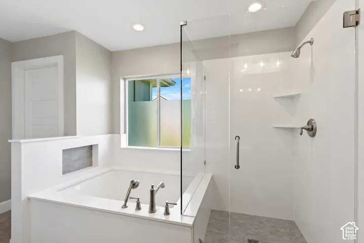 Built-in soaking tub with a metal faucet and handheld sprayer, glass-enclosed shower featuring a metal shower head and integrated shelving, recessed lighting, and a frosted window