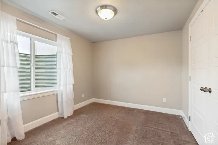 Neutral-toned bedroom featuring wall-to-wall carpeting, an egress window with a metal window well, and plenty of natural light and a generously sized closet