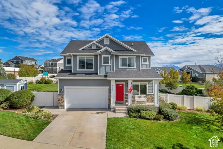 Two-story exterior featuring fiber-cement siding, stone veneer accents, an attached two-car garage, a covered front porch with square columns, and a bright red entry door