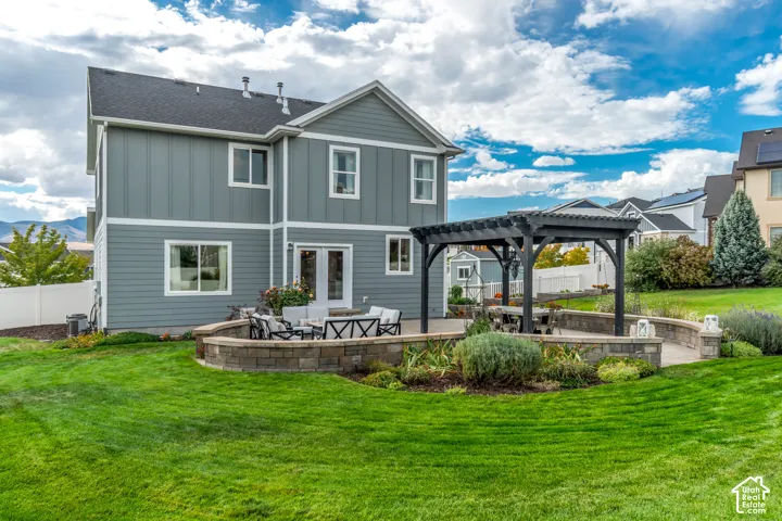 Expansive green lawn, stone-clad retaining wall, dark wood Western Timber Frame pergola, and a generously sized paver patio, surrounded by landscaped garden beds