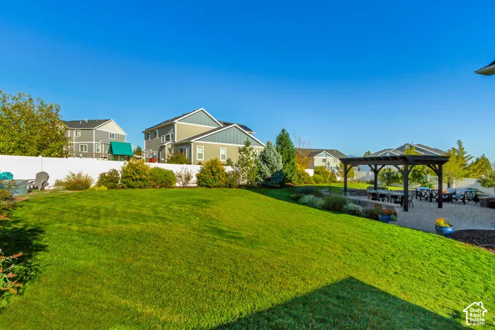 Backyard patio featuring pavers, a Western Timberframe wooden pergola, and a curved stone retaining wall surrounded by beautifully planted garden beds and an expansive grass lawn