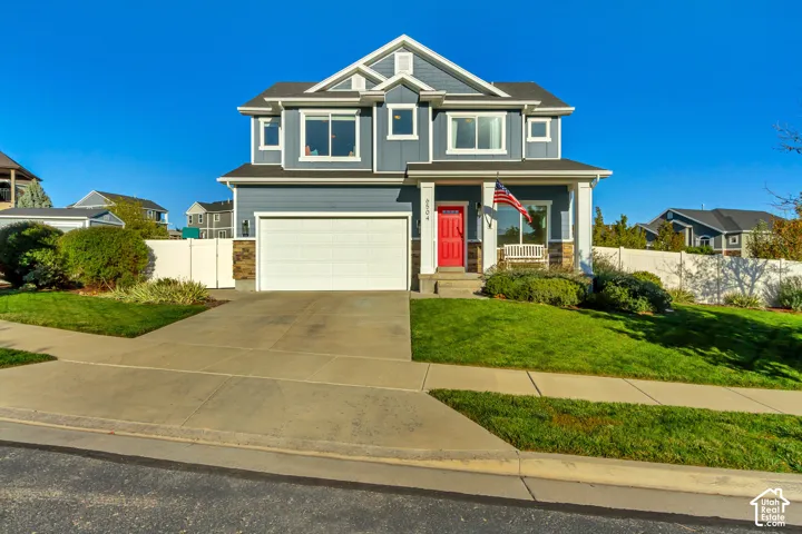 Two-story residence featuring full wrap gray James Hardie cement board siding with stone veneer accents, a covered front porch, a red entry door, and a two-car garage
