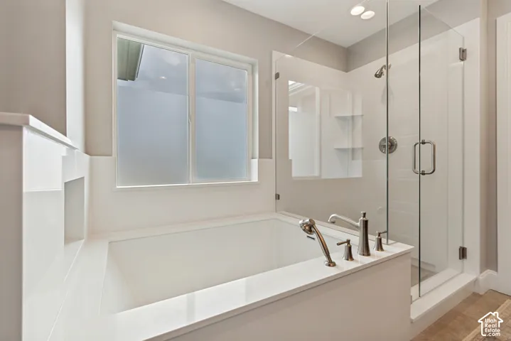 Generously sized soaking bathtub with deck-mounted fixtures, separate euroglass-enclosed shower, quartz surround and frosted window