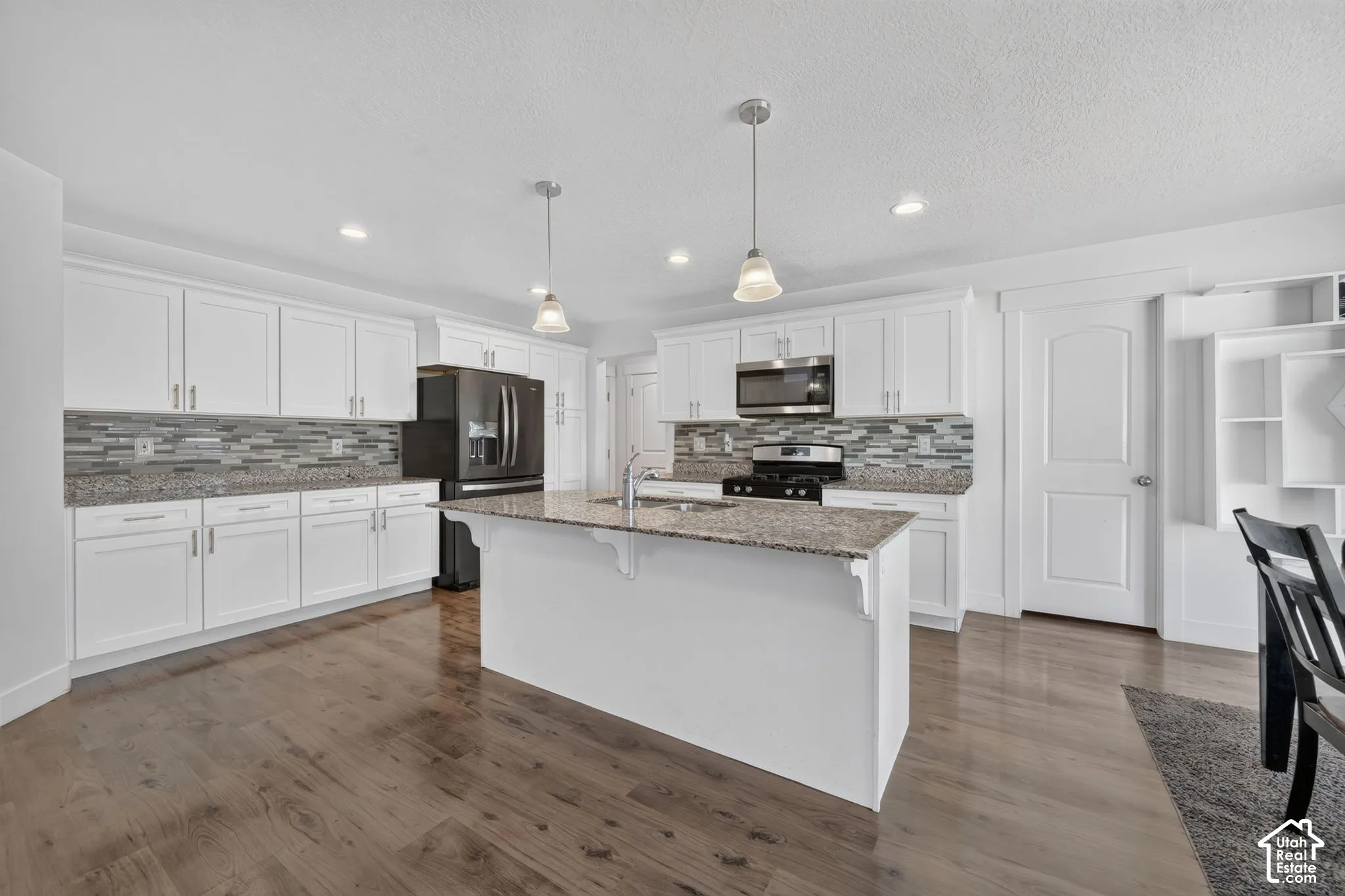 Chef's kitchen featuring white cabinetry, stainless steel appliances, a large island with granite countertop, pendant lighting, and a geometric tile backsplash