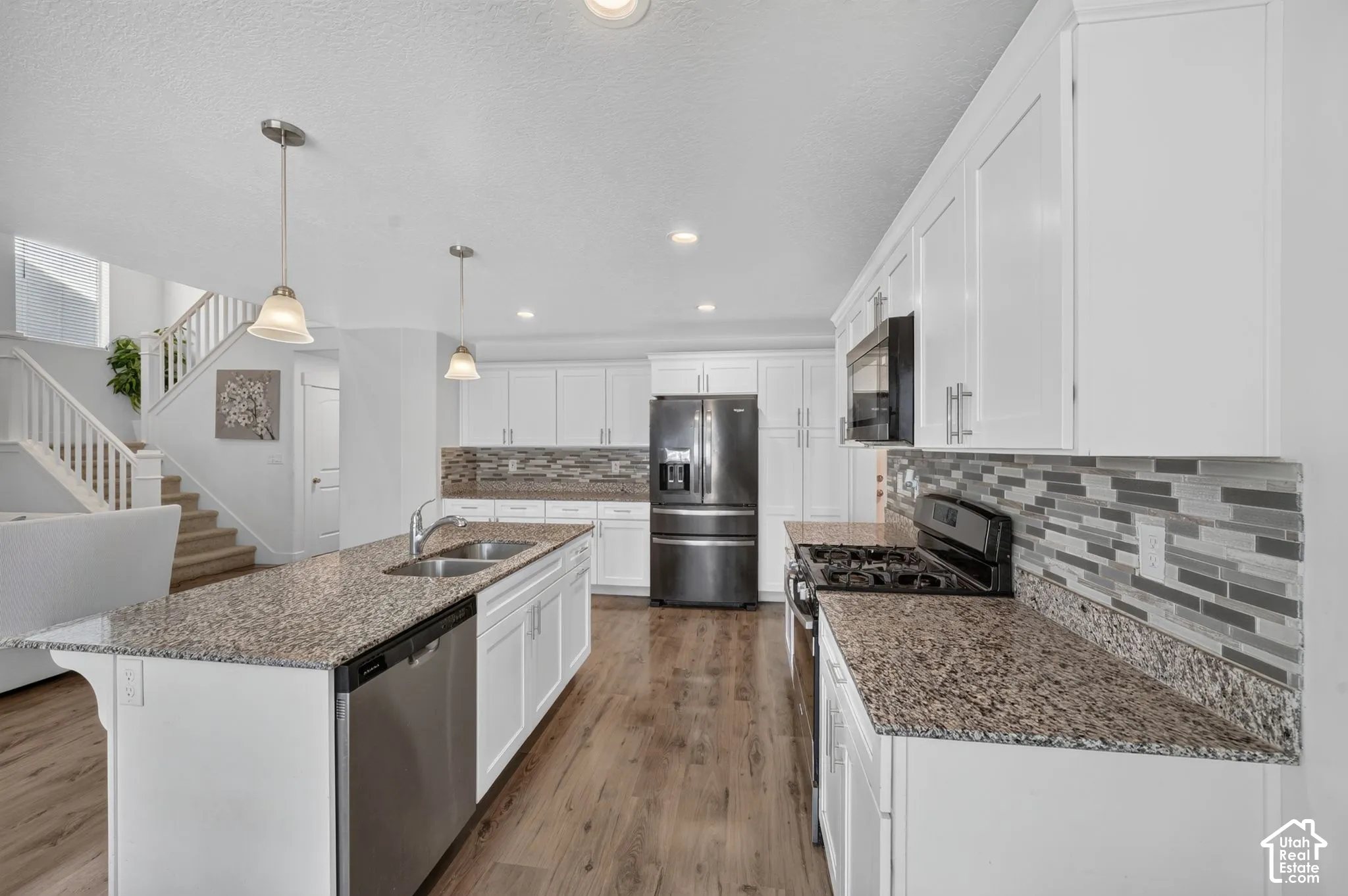 Chef's kitchen showcasing white cabinetry with quartz countertops, stainless steel appliances including a French-door refrigerator, dual pendant lighting over the island, and a geometric tile backsplash