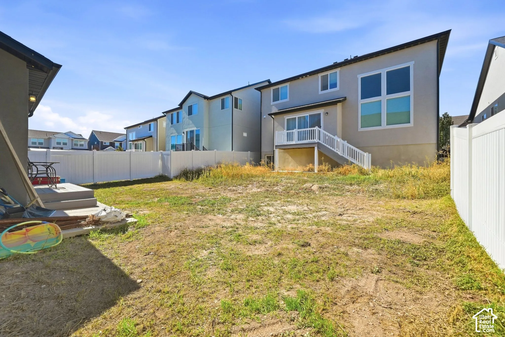 Expansive backyard with a level lawn area, white vinyl privacy fencing, and concrete patio