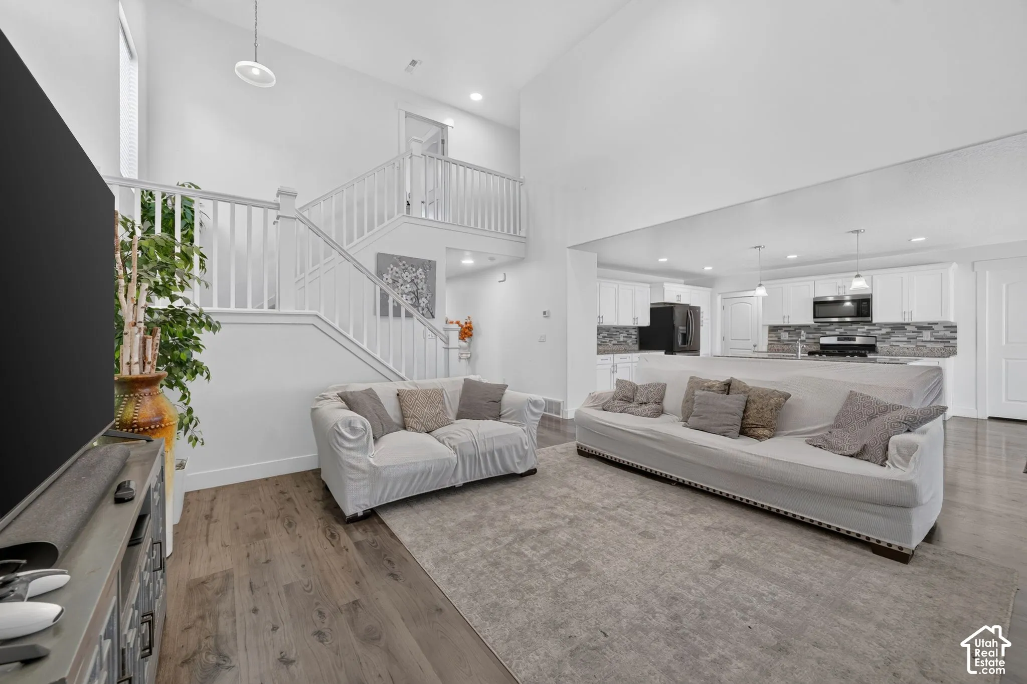 Vaulted ceiling living area featuring wood-finish flooring and a staircase with white railings