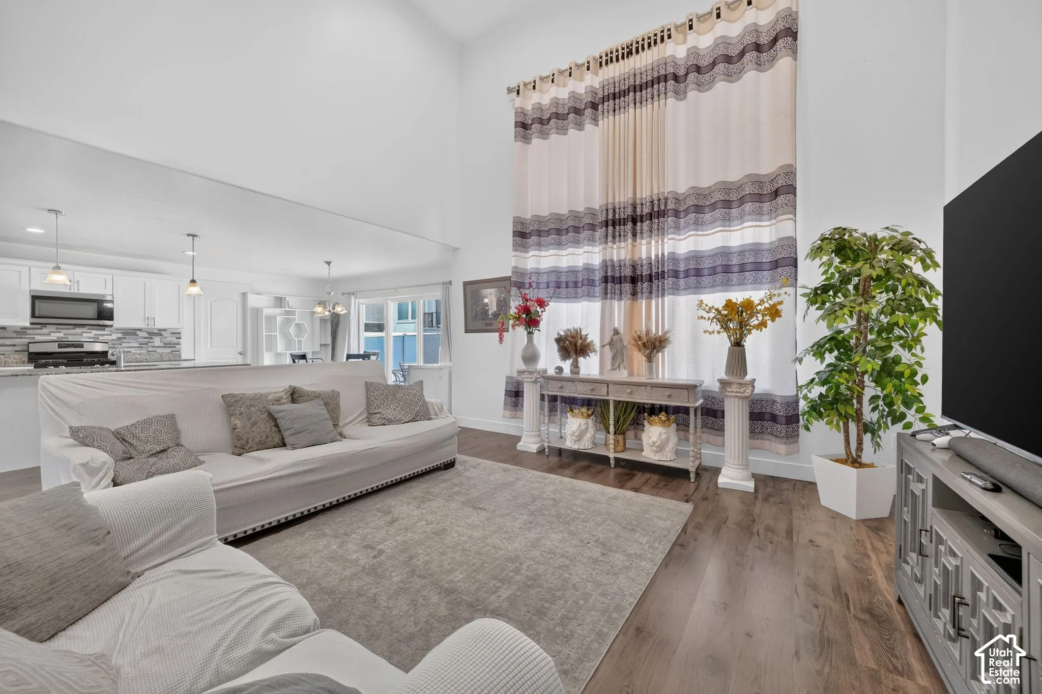 Vaulted ceiling enhancing the open concept layout, wood-finish flooring, and white cabinetry in the kitchen featuring a tile backsplash