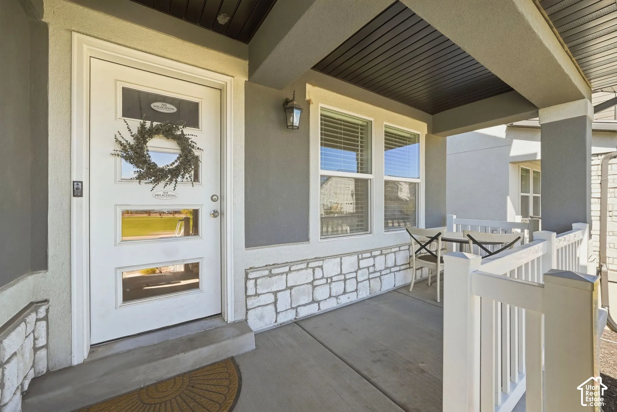 Covered front porch featuring a white entry door with glass inserts, stone veneer detailing, and exterior lighting