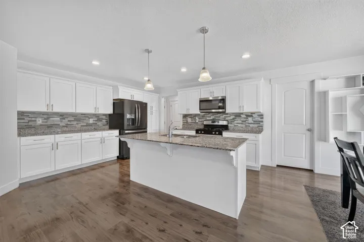 Chef's kitchen featuring white cabinetry, stainless steel appliances, a large island with granite countertop, pendant lighting, and a geometric tile backsplash