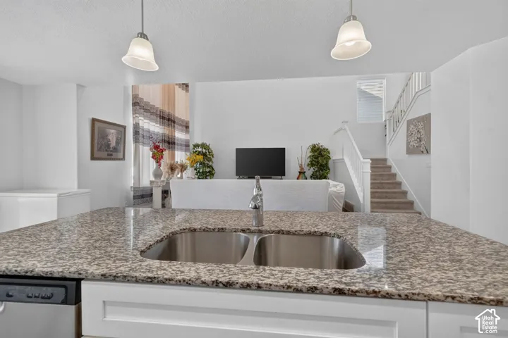 Open-concept kitchen and living area featuring a granite-topped island with dual undermount sinks, stainless steel appliances, pendant lighting, and white cabinetry