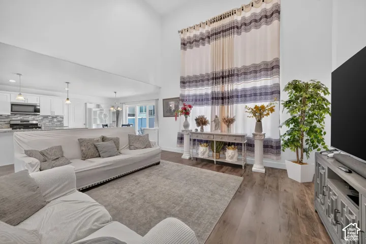 Vaulted ceiling enhancing the open concept layout, wood-finish flooring, and white cabinetry in the kitchen featuring a tile backsplash