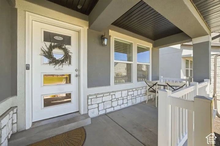 Covered front porch featuring a white entry door with glass inserts, stone veneer detailing, and exterior lighting