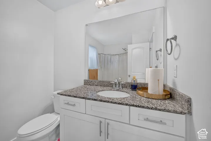 White vanity with shaker-style cabinetry, granite-finish countertop, and undermount sink