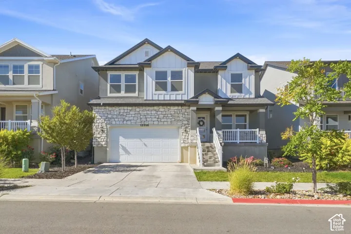 Contemporary exterior featuring a stone and siding facade, an attached two-car garage, a covered front porch with white railings, and mature landscaping