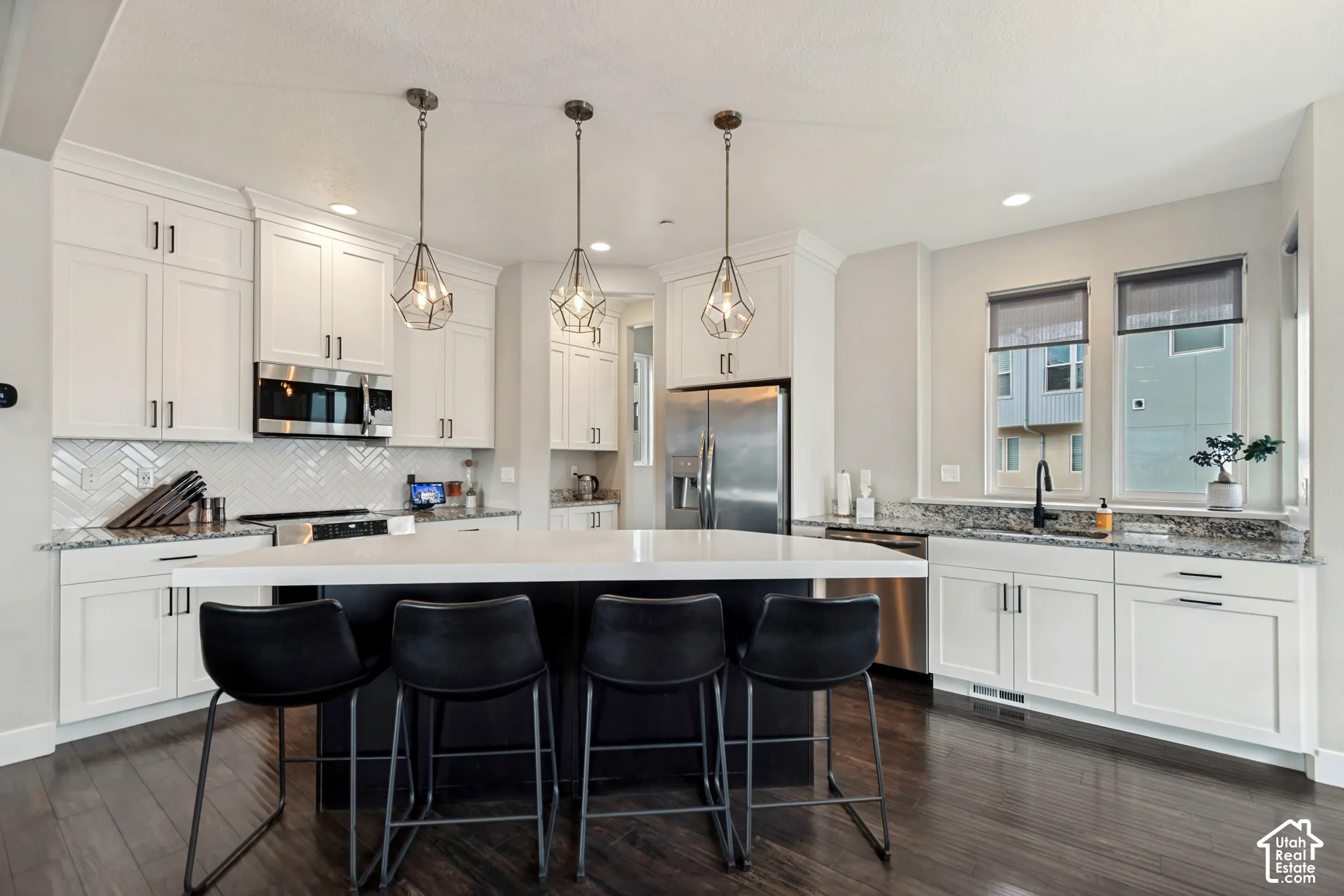 Kitchen featuring a large island with seating, white shaker-style cabinetry, stainless steel appliances, and wood-finish flooring