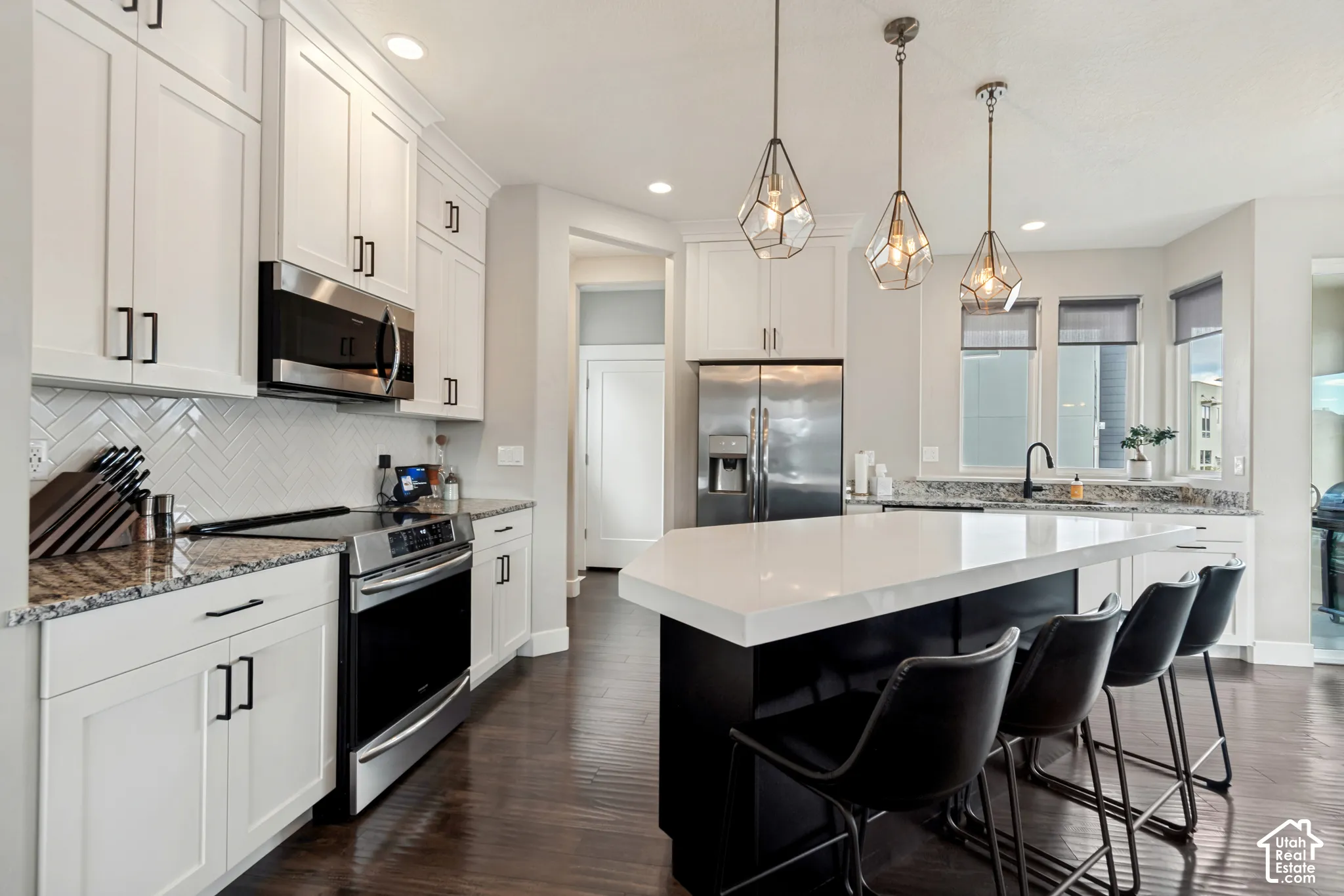 Gourmet kitchen featuring white shaker cabinets, stainless steel appliances, granite countertops, a large center island with quartz countertop, and wood-finish flooring