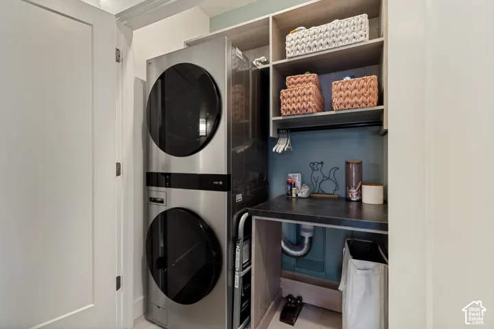 Stainless steel stacked washer and dryer unit, built-in shelving, dark countertop, and light-colored cabinetry