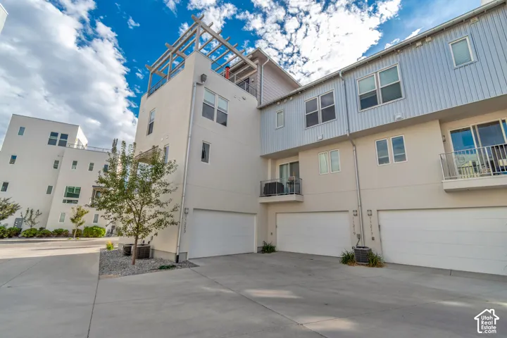 Modern townhome architecture featuring multiple garage doors, balconies with metal railings, and a rooftop pergola