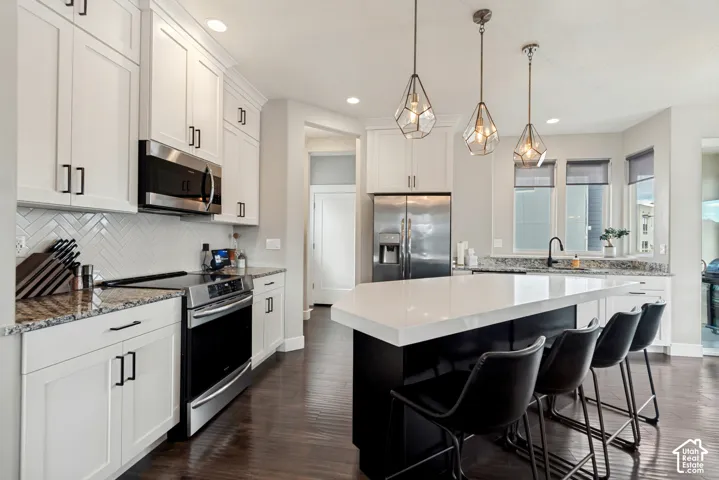 Gourmet kitchen featuring white shaker cabinets, stainless steel appliances, granite countertops, a large center island with quartz countertop, and wood-finish flooring