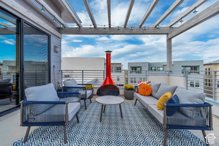 Private rooftop patio with a wooden pergola, sliding glass door access, exterior wall lighting, and horizontal metal railings