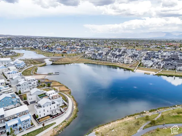 Aerial overview of a community featuring a central lake with a bridge, surrounding residential properties, and a paved pathway system