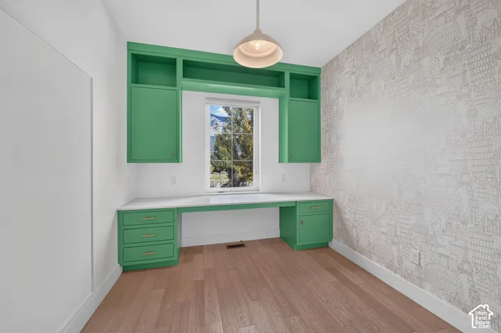 Second home office - built-in cabinetry with a desk surface, wood-finish flooring, accent wall, and a central window