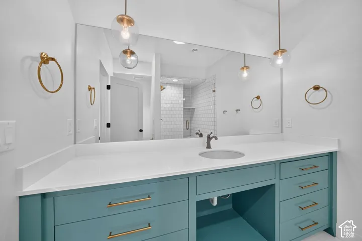 Dual pendant lighting fixtures, a large vanity mirror, an undermount sink with a bronze-finish faucet, a white countertop, and a teal vanity with brass-finish hardware