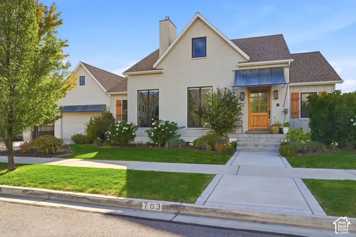 White brick exterior with a wood entry door, metal awning, and mature landscaping