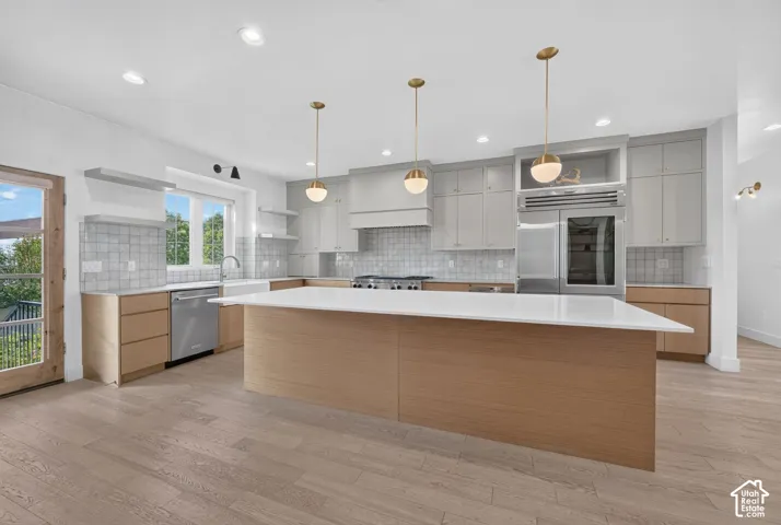 Gourmet kitchen featuring a large central island, light wood-finish flooring, stainless steel appliances, modern pendant lighting, and a farmhouse sink