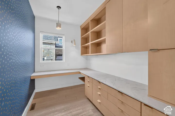 Built-in desk with a light-toned countertop, wood-finish cabinetry, open shelving, and wood-finish flooring