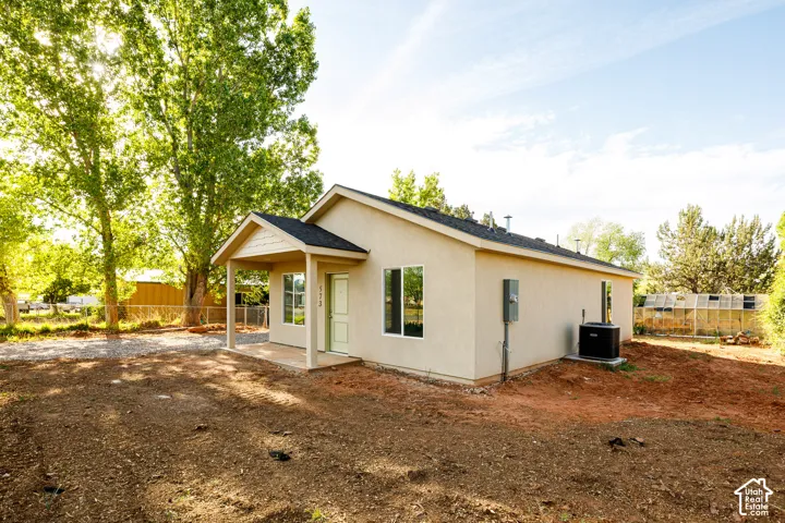 Stucco exterior featuring a covered front porch, dark shingle roofing, and an integrated heating and cooling unit