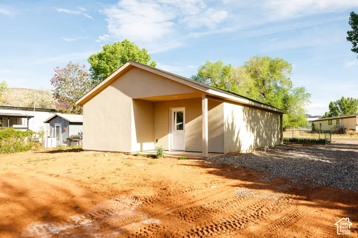 Stucco-finish exterior featuring a covered porch with support pillar and gravel-surfaced lot