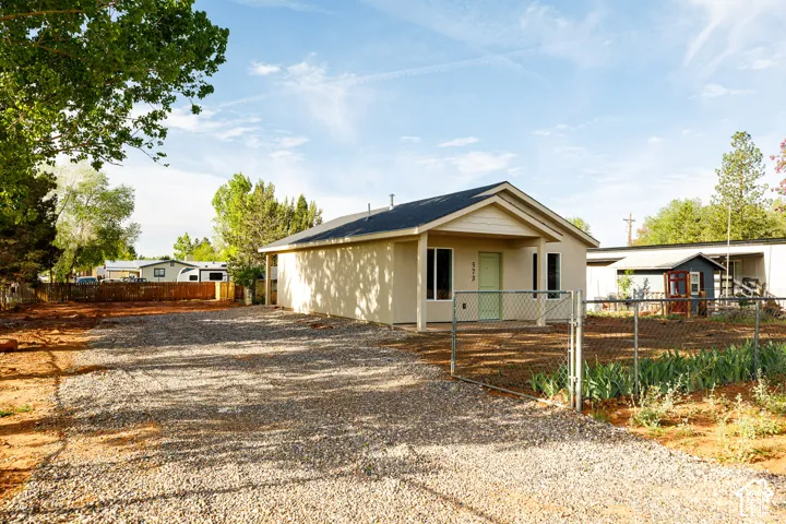 Single-story exterior featuring neutral-toned stucco siding, a covered front porch, a pitched roof, and a gravel driveway