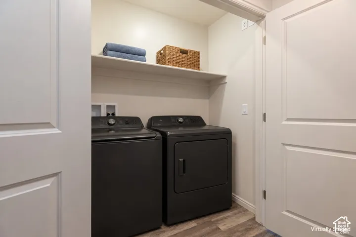 Washer and Dryer do not convey. Laundry area featuring wood-finish flooring, a white-painted overhead storage shelf, and double-panel doors