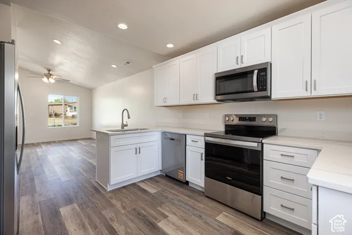 Kitchen featuring white shaker-style cabinetry, quartz countertops, stainless steel appliances, wood-finish flooring, and recessed lighting